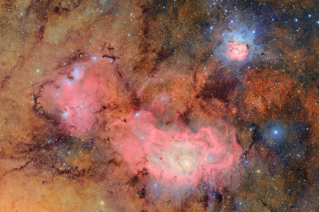 Fototografia das nuvens de gás e poeira que compõem a nebulosa Trífida (canto superior direito) e a nebulosa Lagoa, que estão a milhares de anos-luz de distância da Terra, podem ser vistas.