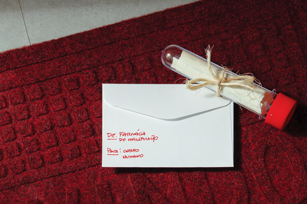 Imagem de um envelope branco e um tubo de plástico em cima de um tapete vermelho.