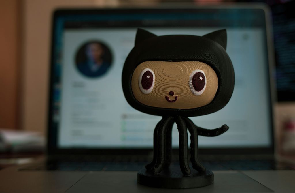 Boneco do logo do GitHub na frente de um notebook desfocado ao fundo