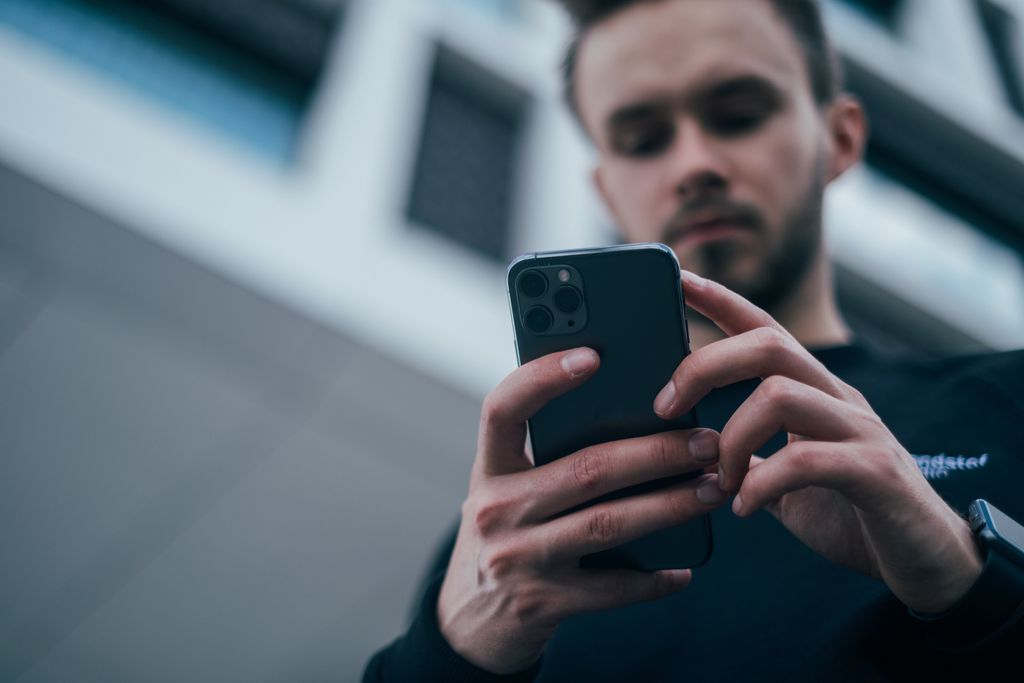 Homem desfocado ao fundo segura um celular em primeiro plano