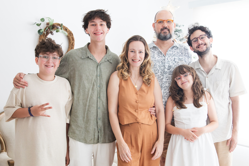 Imagem, em fundo branco, de uma família reunida. Vê-se o pai, a mãe e três filhos e uma filha. Todos estão sorrindo.