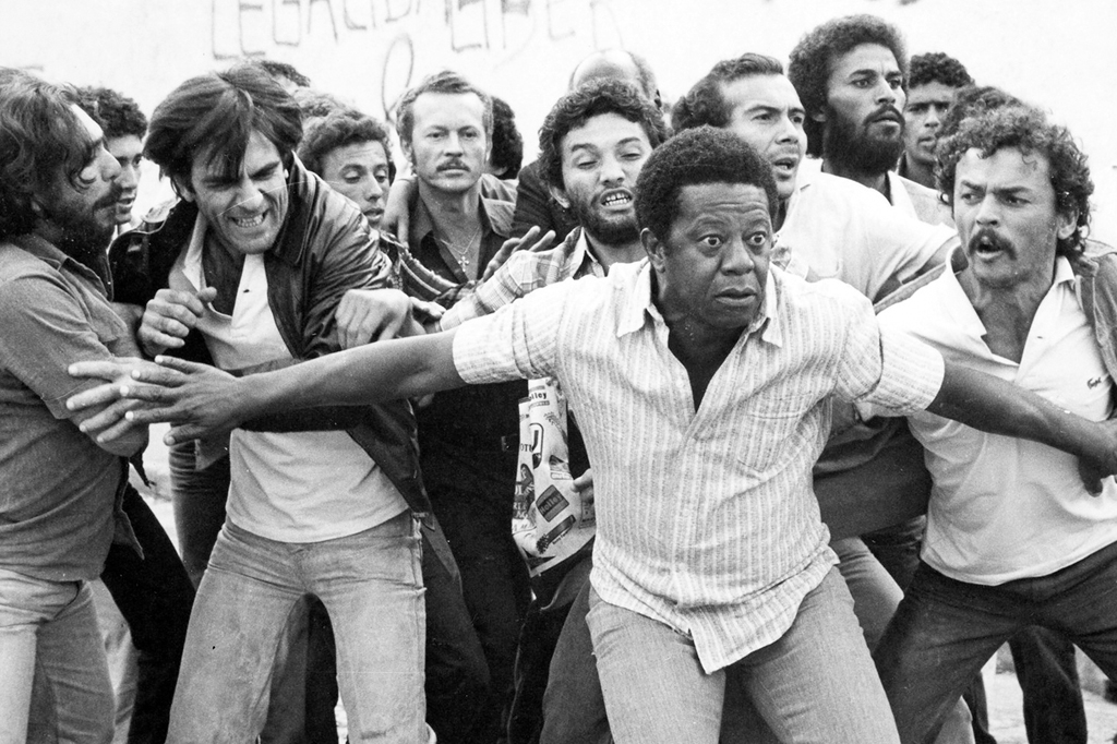 Imagem com cena do filme Eles Não Usam Black-Tie (1981). Vê-se operários exaltados reunidos durante uma greve.