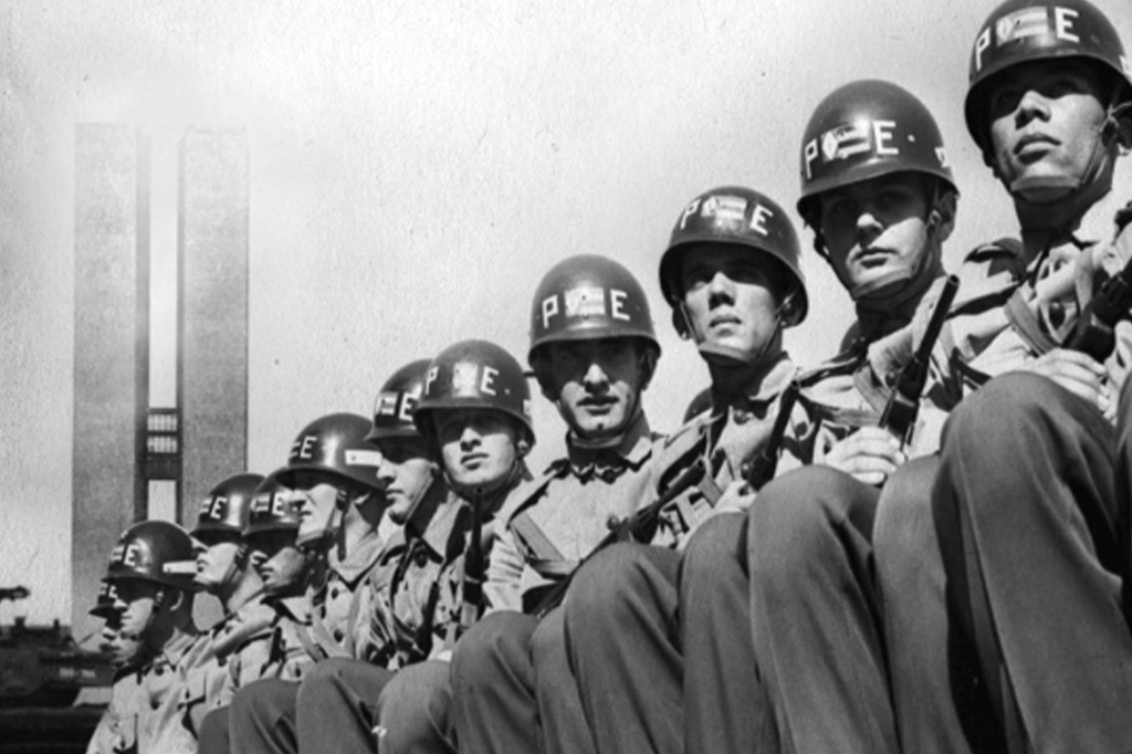 Imagem com cena do filme O Dia que Durou 21 Anos (2012). Vê-se um grupo de policiais do exército perfilados. Ao fundo, o prédio do Congresso Nacional.