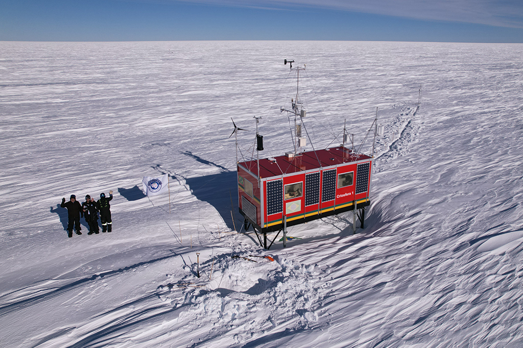 Fotografia aérea da estação da missão criosfera ao lado de três cientistas.