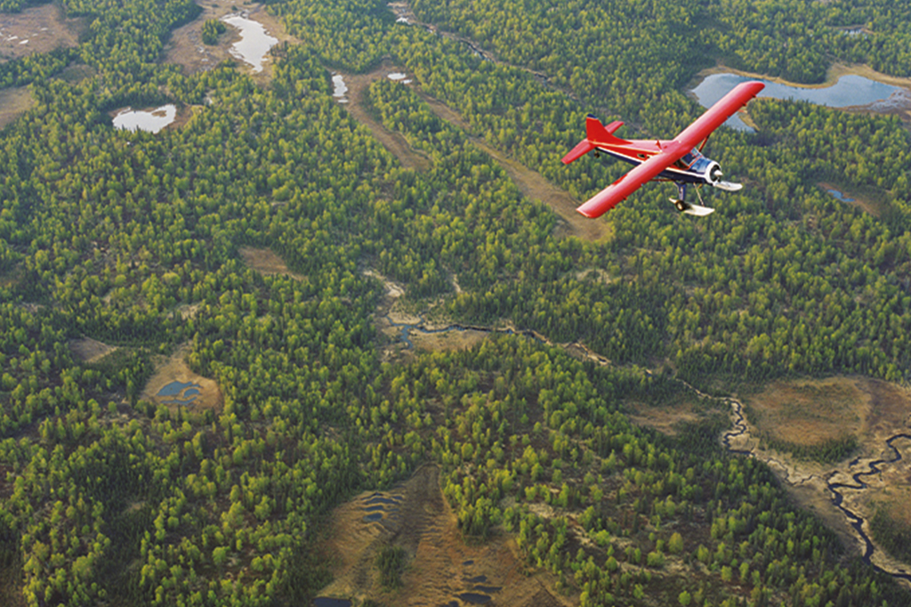 Imagem de uma hidroavião vermelho sobrevoando uma região de difícil acesso na floresta amazônica.