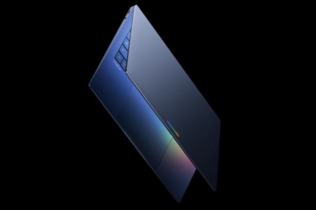 Notebook azul-marinho com teclado e tela parcialmente abertos, exibindo um touchpad com reflexos coloridos e botões de função na lateral esquerda do teclado, sobre fundo preto.