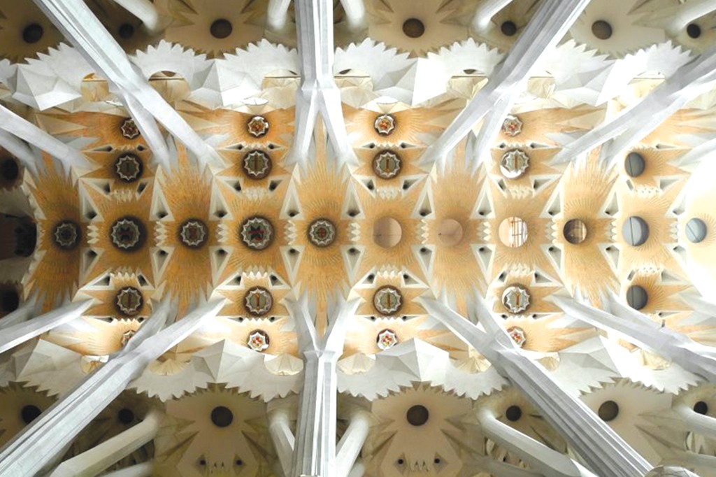 Teto de uma igreja com colunas brancas que se ramificam, sustentando painéis geométricos em tons de bege e branco, com detalhes circulares e estrelados
