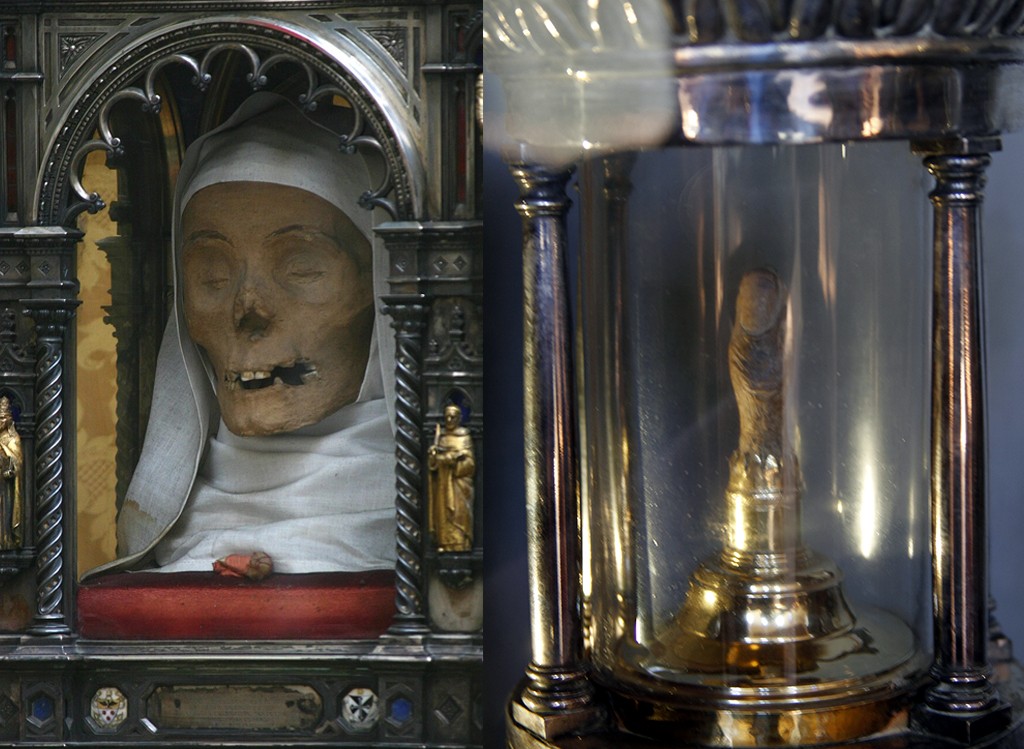À esquerda, um crânio mumificado com pele ressecada e boca aberta, envolto em tecido branco, dentro de um relicário prateado ornamentado. À direita, um dedo mumificado em um recipiente de vidro cilíndrico, com base dourada, ladeado por colunas metálicas