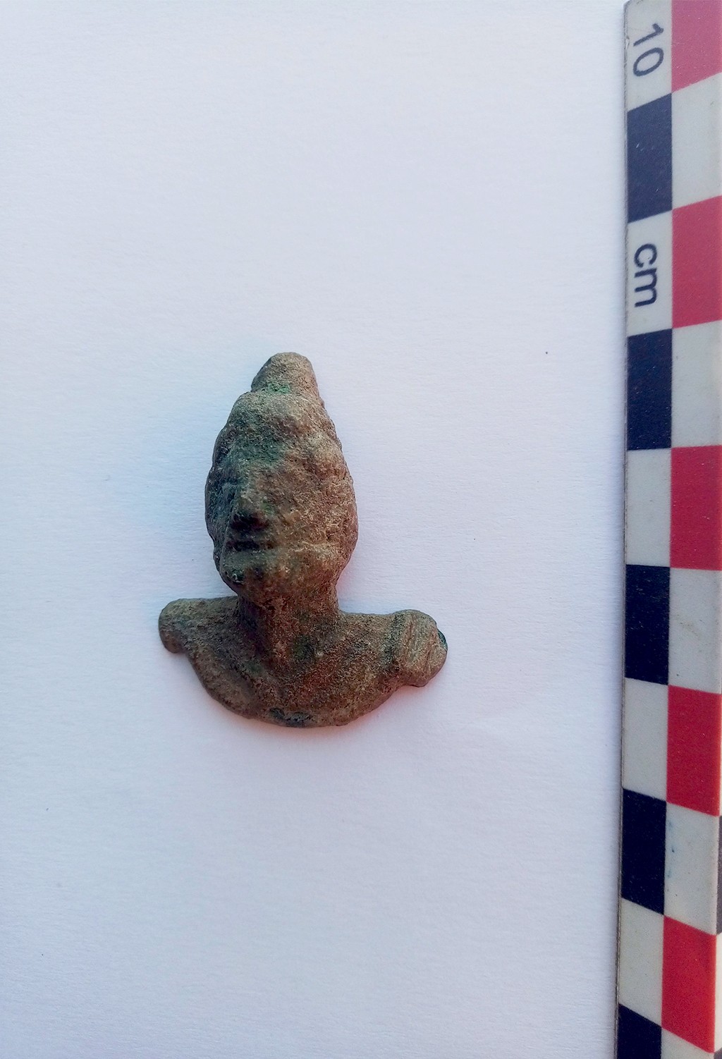 Estatueta antiga de bronze com cabeça e ombros, representando Odisseu, com textura rugosa e coloração esverdeada, sobre fundo branco com régua vertical de 10 cm à direita