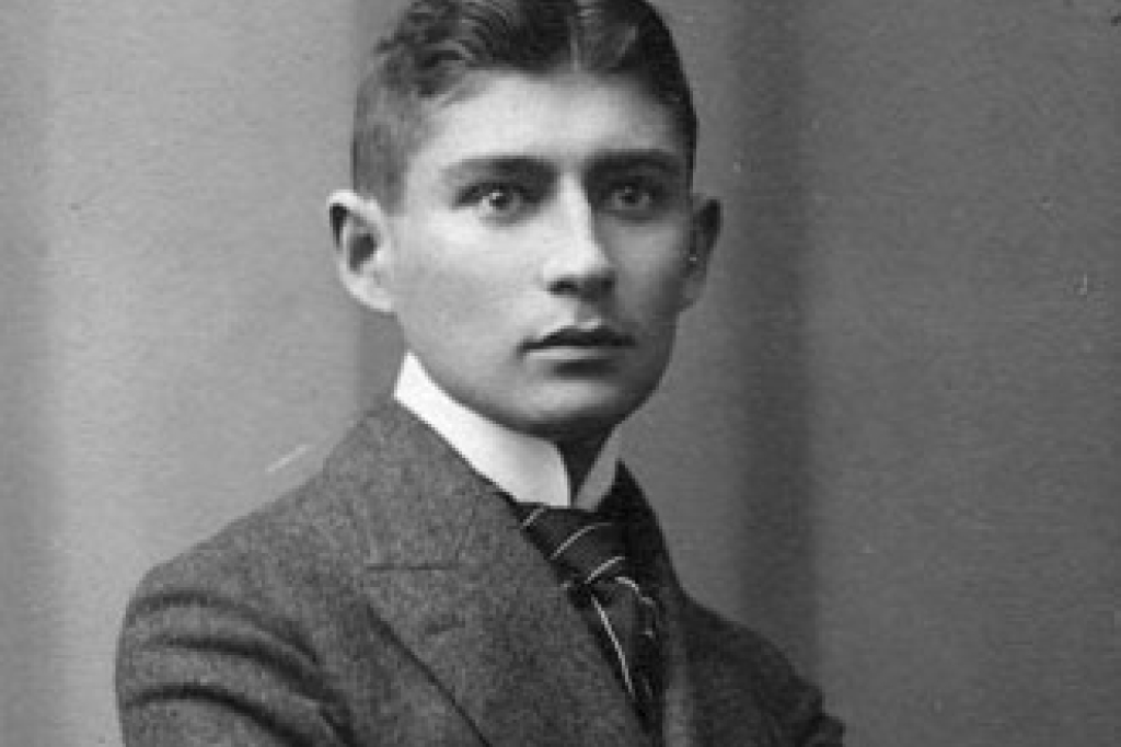 Fotografia de um homem magro e branco, Franz Kafka, em preto e branco. Ele está de terno. Só conseguimos ver do peito para cima.