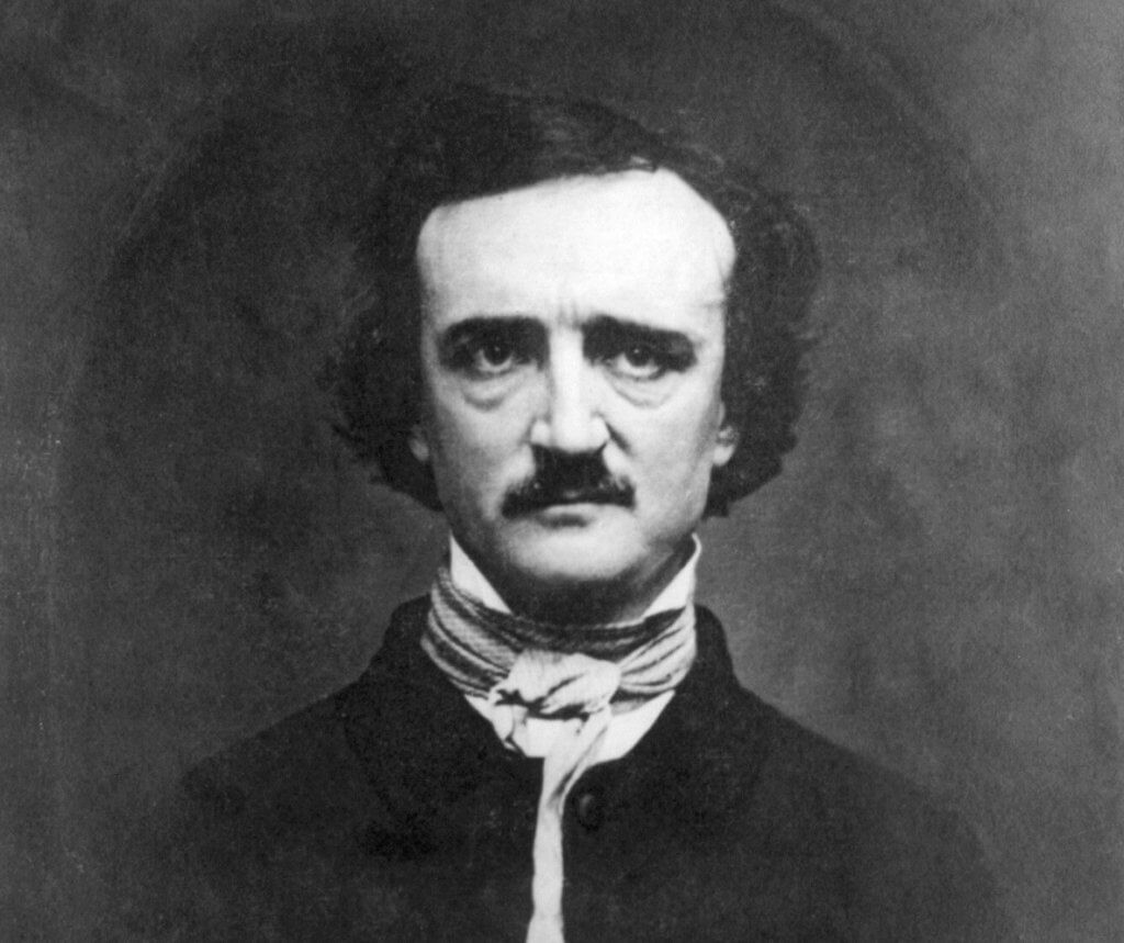 Retrato em preto e branco de Edgar Allan Poe, com cabelos escuros e ondulados, bigode e olhos profundos. Ele veste um casaco escuro e um lenço listrado no pescoço, amarrado em um laço frontal. A expressão é séria, com a cabeça ligeiramente inclinada para a frente