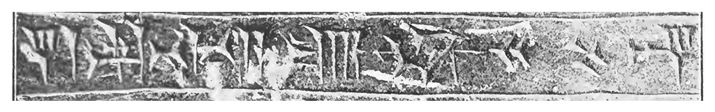 Inscrição antiga em baixo-relevo, com caracteres em estilo cuneiforme ou hieroglífico, gravados em uma superfície retangular de pedra ou argila. A textura da superfície é rugosa e irregular, com áreas mais claras e escuras, indicando desgaste e envelhecimento. Os símbolos são complexos e variados, com linhas verticais, horizontais e diagonais, formando um padrão contínuo ao longo da faixa. A imagem está em preto e branco, realçando o contraste entre os relevos e o fundo.