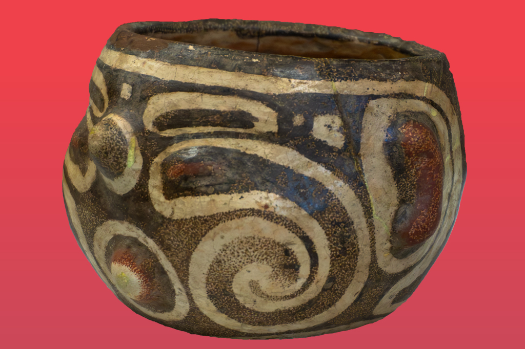Vaso de cerâmica antigo com fundo marrom escuro e padrões espirais em bege claro, com detalhes em azul e manchas avermelhadas. A peça tem uma abertura superior e textura rugosa, sobre um fundo vermelho liso